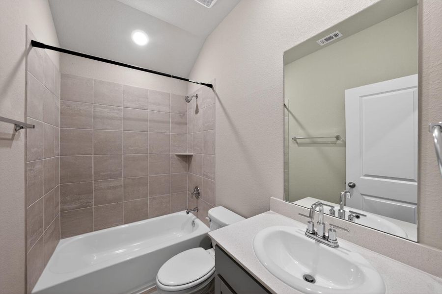 Bathroom featuring vanity, shower / bathtub combination, lofted ceiling, and a textured wall