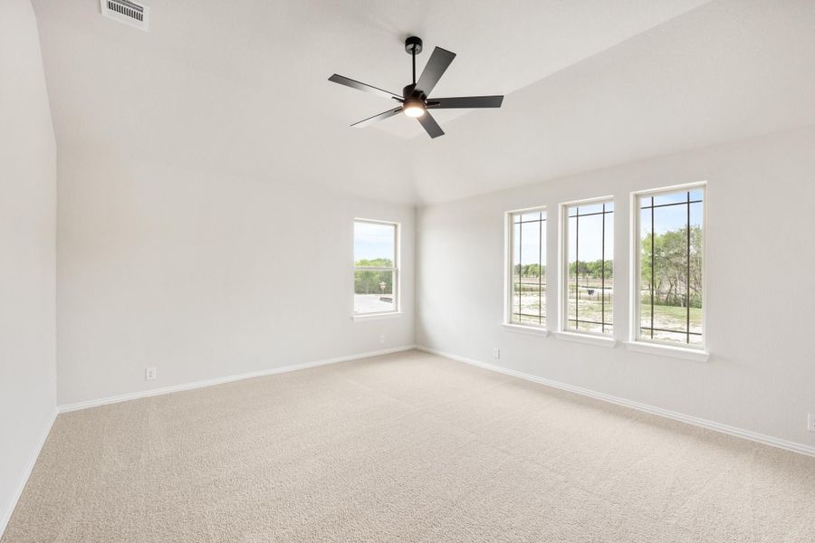 Empty bedroom with vaulted ceiling, black ceiling fan, carpet flooring, and four windows with outdoor views
