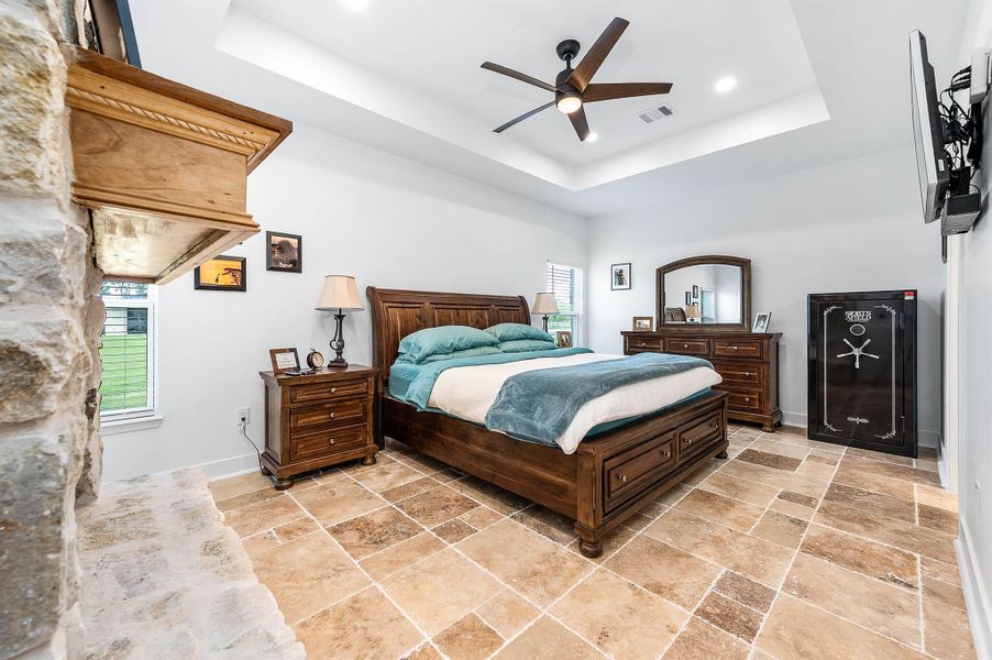 The Primary bedroom features a stunning stone accent wall, tray ceiling with modern lighting and fan, and large windows that fill the room with natural light. The thoughtful design, warm finishes, and generous layout create a comfortable and relaxing private retreat.