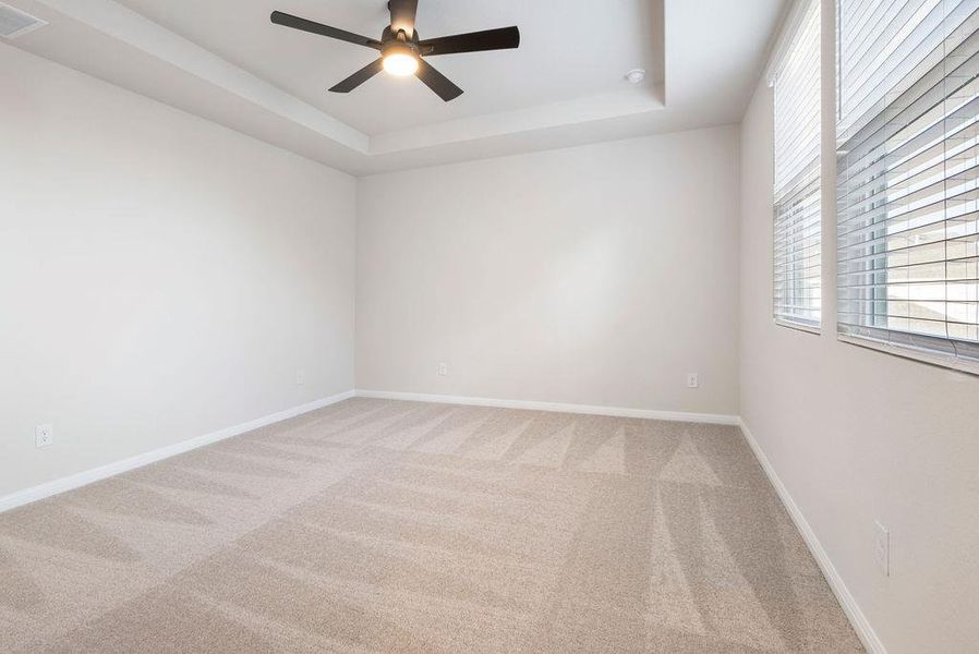 Empty room featuring light colored carpet, ceiling fan, and a tray ceiling