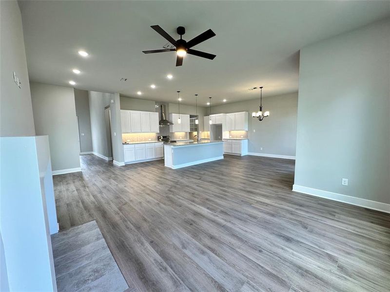 Unfurnished living room with ceiling fan with notable chandelier and hardwood / wood-style flooring