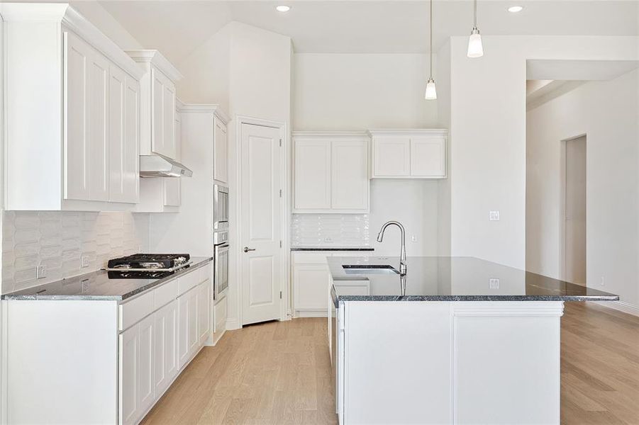 Kitchen featuring light wood-type flooring, backsplash, an island with sink, and appliances with stainless steel finishes