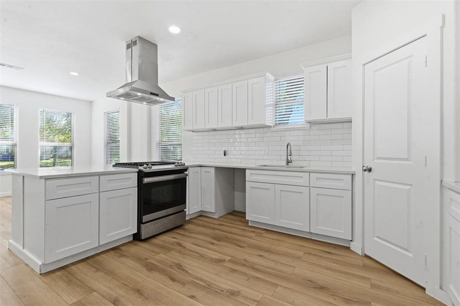 Kitchen featuring white cabinets, decorative backsplash, stainless steel gas range, a peninsula, and island exhaust hood Kitchen featuring white cabinets, decorative backsplash, stainless steel gas range, a peninsula, and island exhaust hood