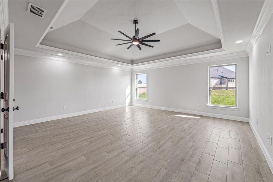 Empty room with a tray ceiling, ornamental molding, wood finish floors, and ceiling fan