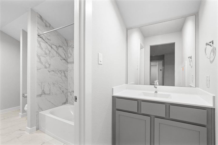 Secondary bath features tile flooring, bath/shower combo with tile surround, stained wood cabinets, beautiful light countertops, mirror, sleek fixtures and modern finishes.