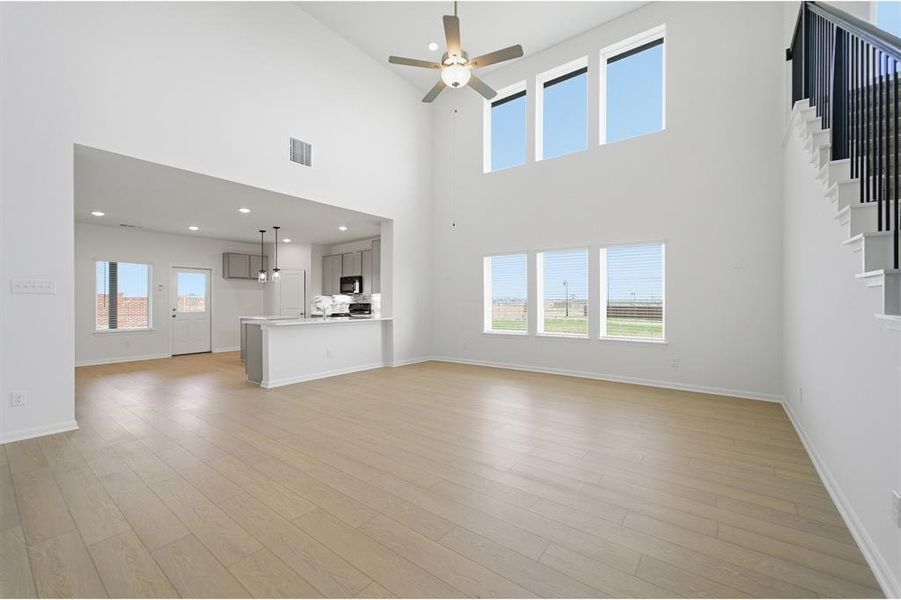 Unfurnished living room featuring a ceiling fan, recessed lighting, light wood finished floors, and a high ceiling