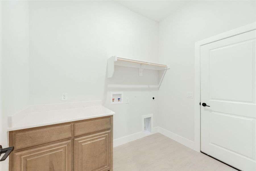 Laundry room with wood cabinet, wall shelf, and washer and dryer hookups on white walls Laundry room with wood cabinet, wall shelf, and washer and dryer hookups on white walls