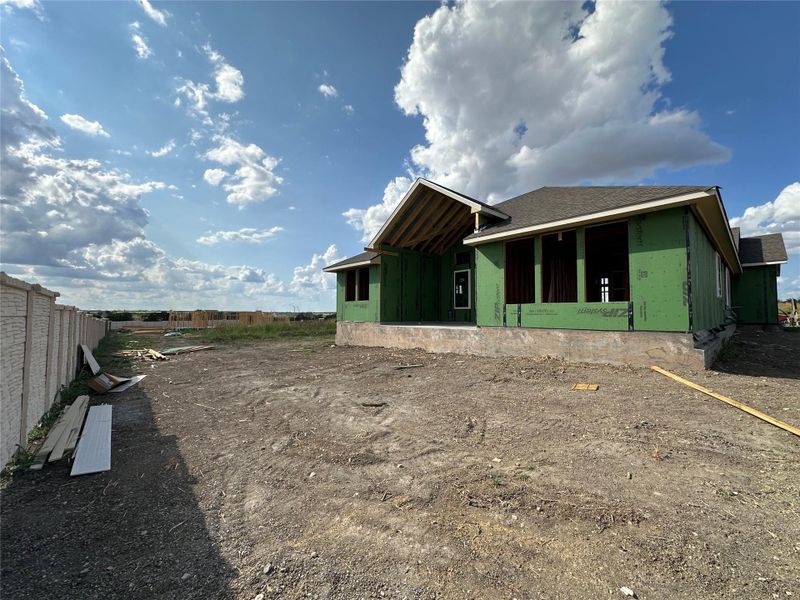 A newly framed residence awaits finishing touches, set against a wide-open horizon under a cloud-streaked sky.
