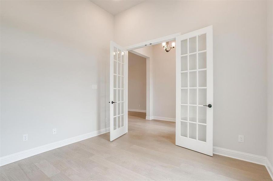 Unfurnished room featuring light hardwood / wood-style floors, french doors, and a notable chandelier