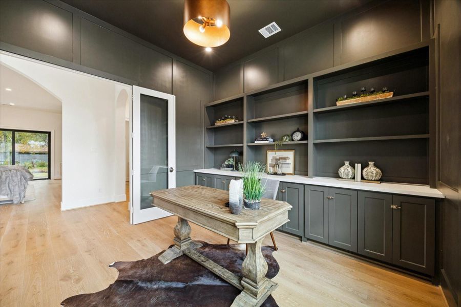 Sophisticated home office with floor-to-ceiling built-ins, glass door entry, and white oak wood flooring.