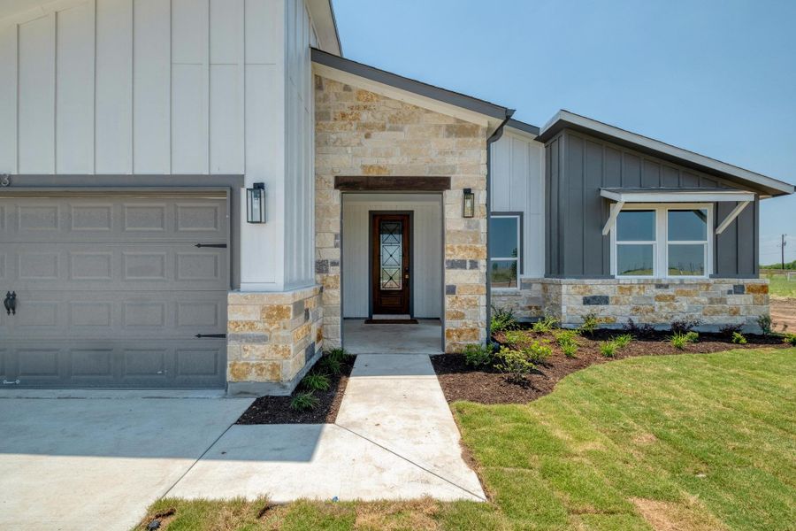 Property entrance featuring board and batten siding, stone siding, an attached garage, a yard, and concrete driveway