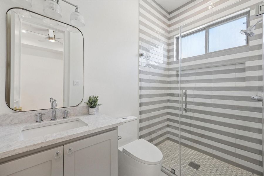 Ensuite bath for the third bedroom features a quartz countertop and Manchester plaid polished marble mosaic tile in the glass enclosed shower.