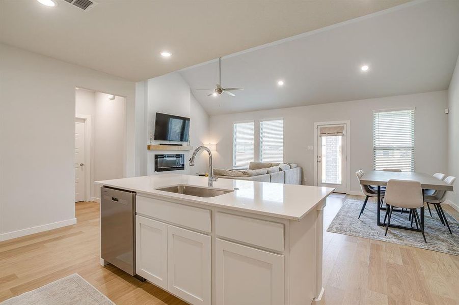 Kitchen featuring white cabinets, open floor plan, light wood-type flooring, a center island with sink, and stainless steel dishwasher Kitchen featuring white cabinets, open floor plan, light wood-type flooring, a center island with sink, and stainless steel dishwasher