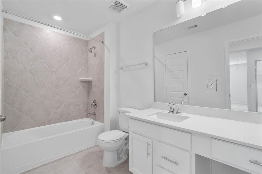 Secondary bath features tile flooring, bath/shower combo with tile surround, stained wood cabinets, beautiful light countertops, mirror, sleek fixtures and modern finishes.