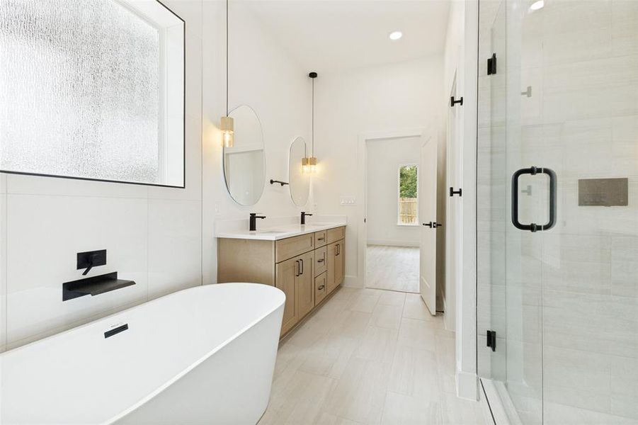 Bathroom featuring a freestanding soaking tub, dual vanity with undermount sinks, frameless glass shower enclosure, and light-toned tile flooring Bathroom featuring a freestanding soaking tub, dual vanity with undermount sinks, frameless glass shower enclosure, and light-toned tile flooring