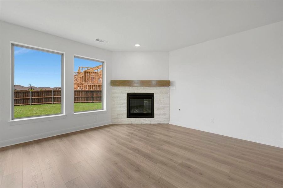 Bright interior featuring wood-finish flooring, a corner fireplace with a stacked stone facade, a wood mantel, and expansive windows