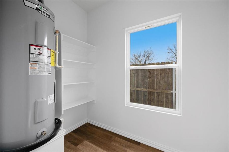 Laundry room with built-in shelving for storage and natural light. Dedicated utility space with water heater and functional layout.