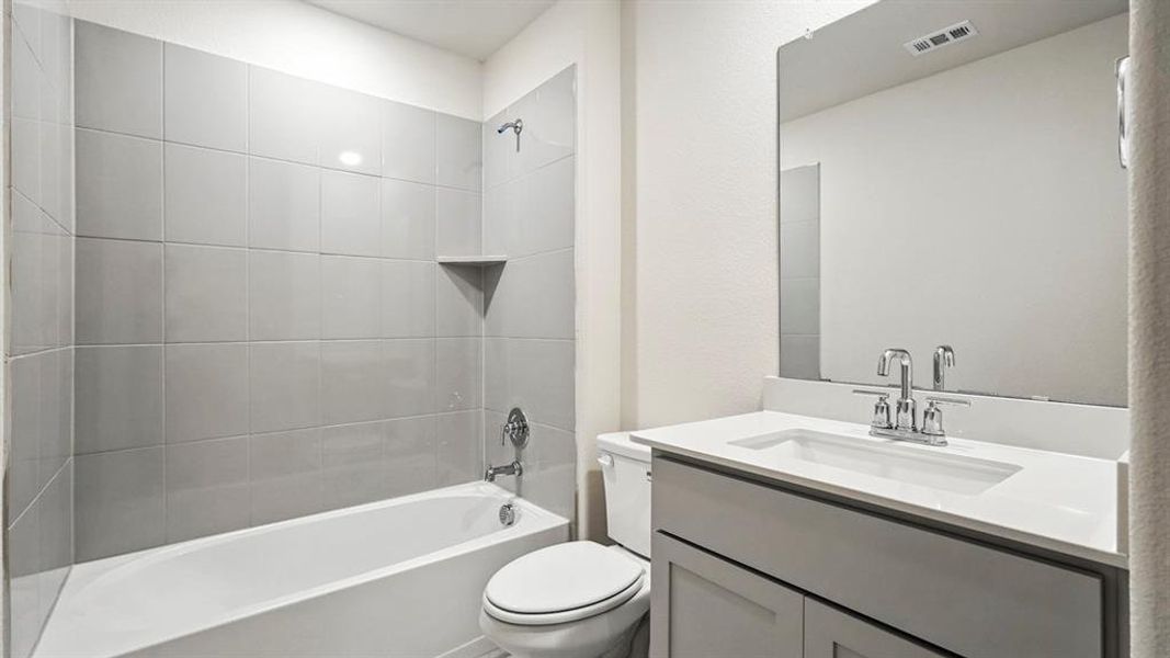 Bathroom featuring a built-in tub with light grey subway tile surround, a built-in shower niche, a vanity with a white countertop and integrated sink, and a chrome faucet