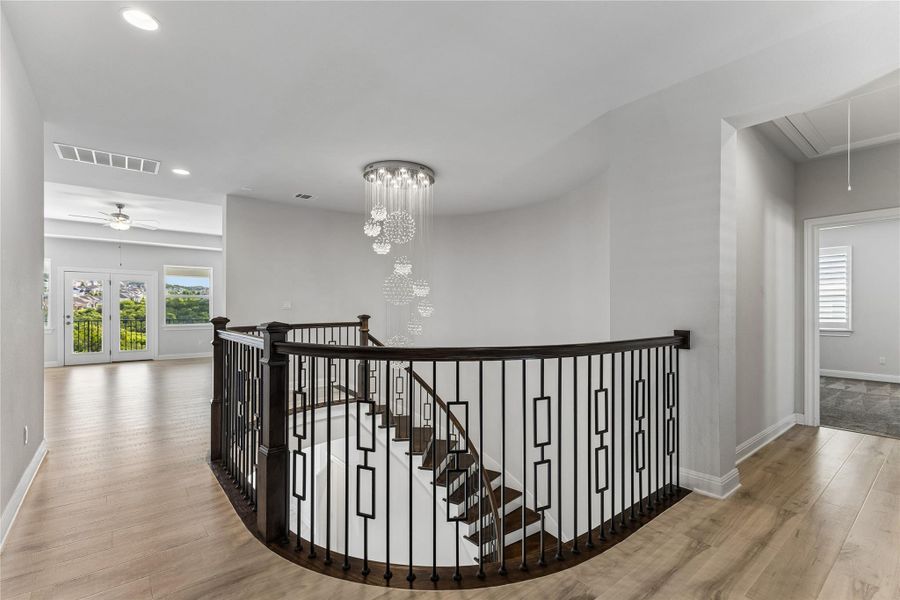 Elegant dark wood and iron railing frames the grand staircase, illuminated by a multi-tiered chandelier.