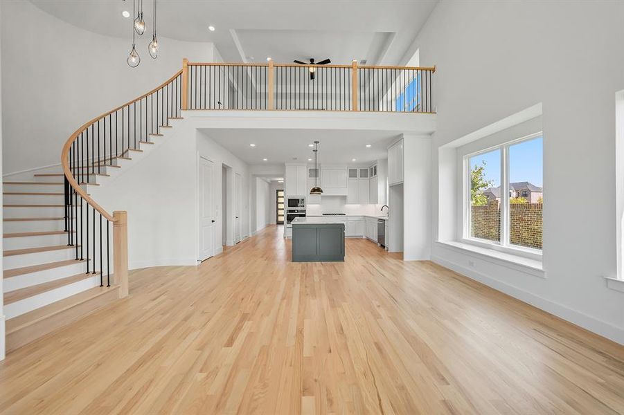 Unfurnished living room featuring a high ceiling, stairway, light wood-style flooring, and recessed lighting