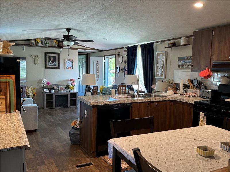 Kitchen with open floor plan, a peninsula, dark wood finish cabinetry, ceiling fan, and black appliances