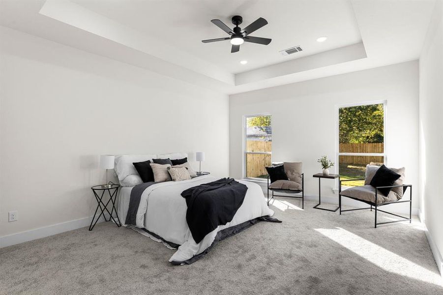 Carpeted bedroom featuring ceiling fan and a raised ceiling