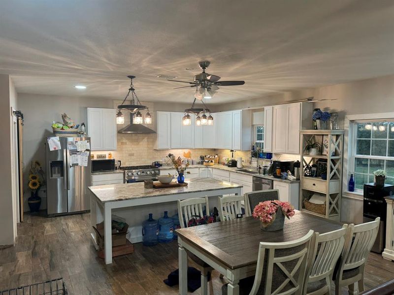 Kitchen featuring stainless steel appliances, light stone countertops, decorative backsplash, white cabinetry, and pendant lighting Kitchen featuring stainless steel appliances, light stone countertops, decorative backsplash, white cabinetry, and pendant lighting