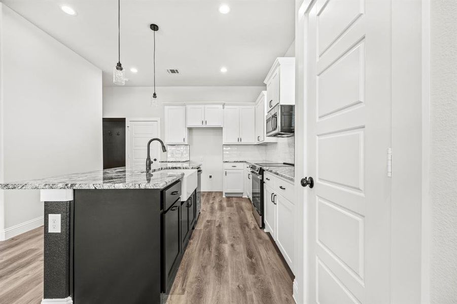 Kitchen with white cabinets, stainless steel appliances, light hardwood / wood-style floors, and an island with sink