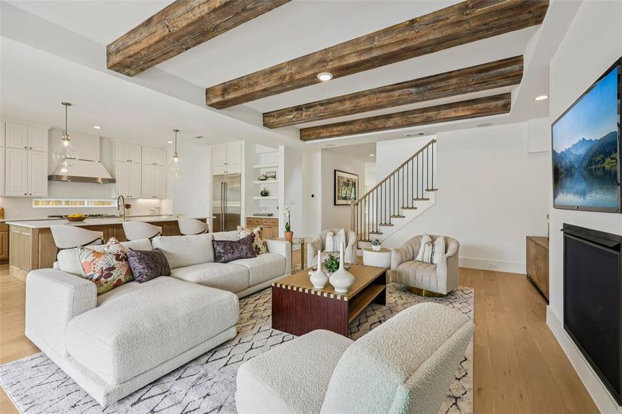 Open-concept living space featuring exposed wood ceiling beams, wood-finish flooring, and a modern kitchen with a large island and stainless steel appliances