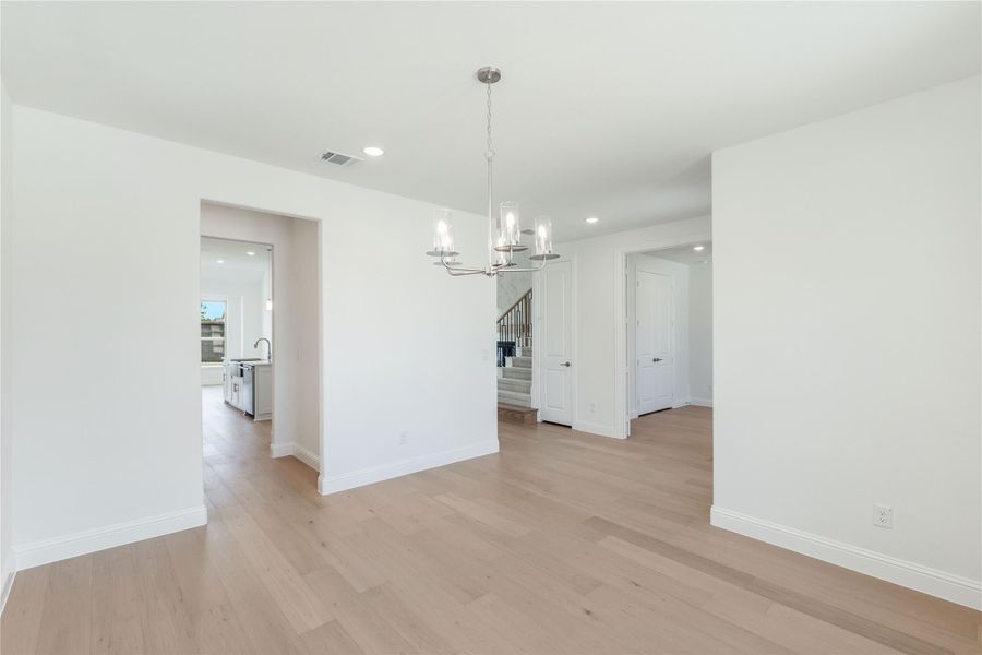 Empty dining room with light hardwood floors, chandelier, and open view to kitchen and staircase