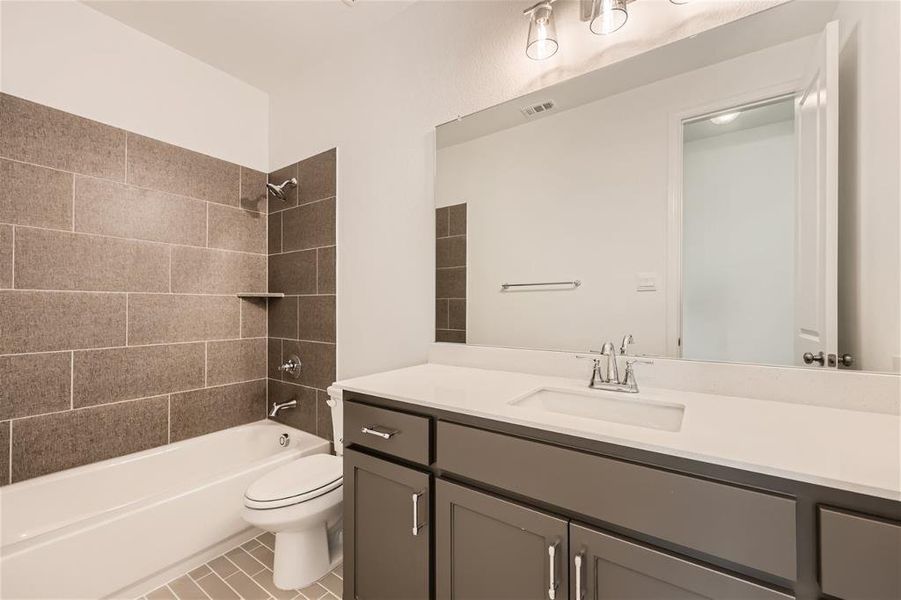 Full bathroom featuring oversized vanity, toilet, tiled shower / bath combo, and tile floors