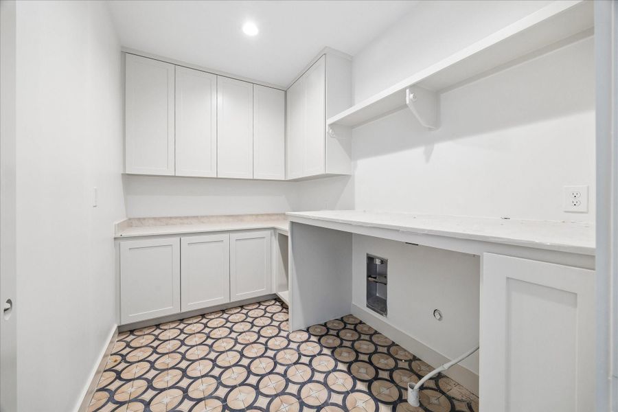 Well designed upstairs utility room offering abundant storage and workspace with extended cabinetry, upper storage, and a dedicated folding counter. The patterned tile flooring adds visual interest while the functional layout provides space for a full size washer and dryer, making everyday tasks both efficient and convenient.