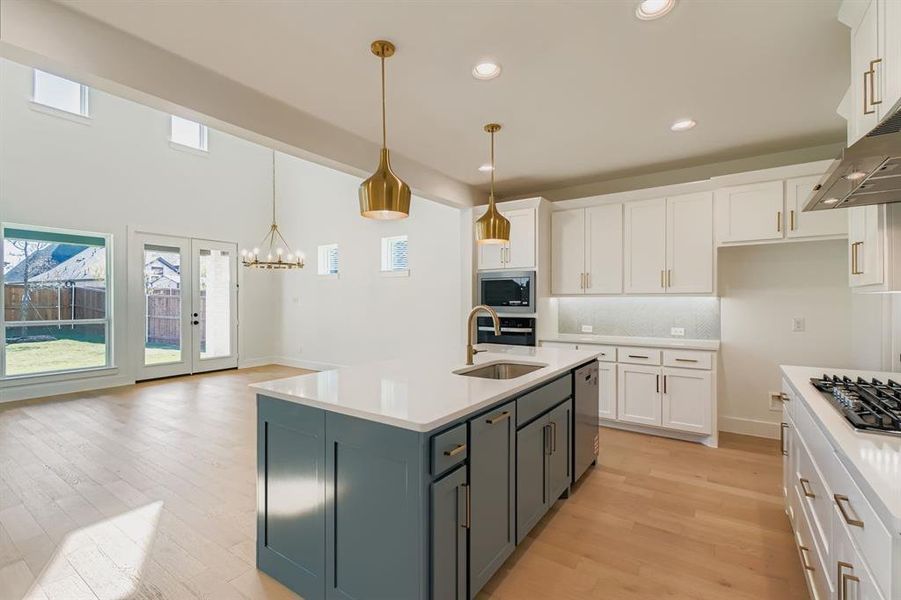 Kitchen with white cabinetry, hanging light fixtures, tasteful backsplash, light wood-style flooring, and stainless steel appliances