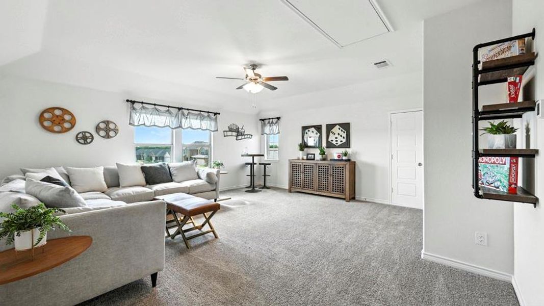This expansive living area features light gray carpeting, multiple windows providing natural light, and a ceiling fan