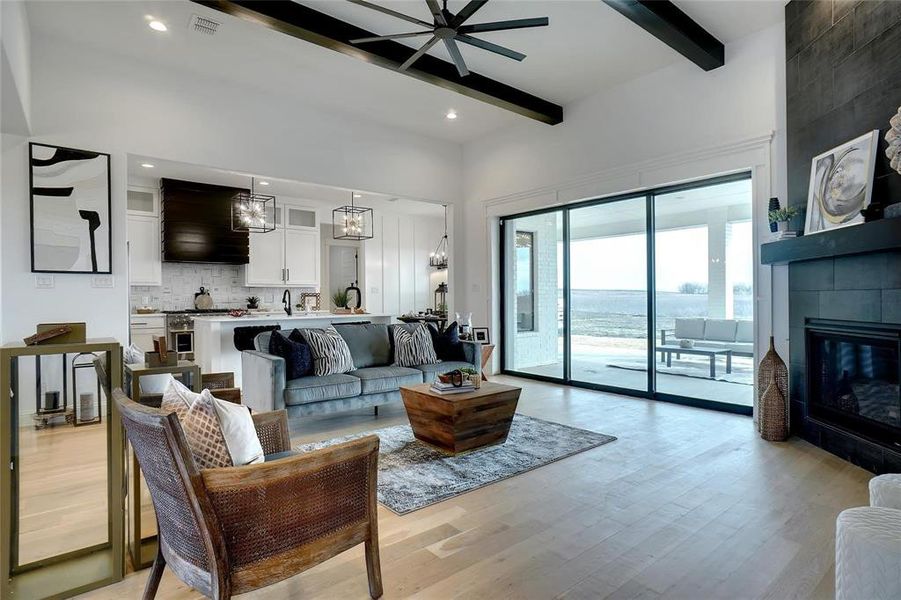 Living room with light wood-style flooring, beam ceiling, a tile fireplace, a chandelier, and a ceiling fan
