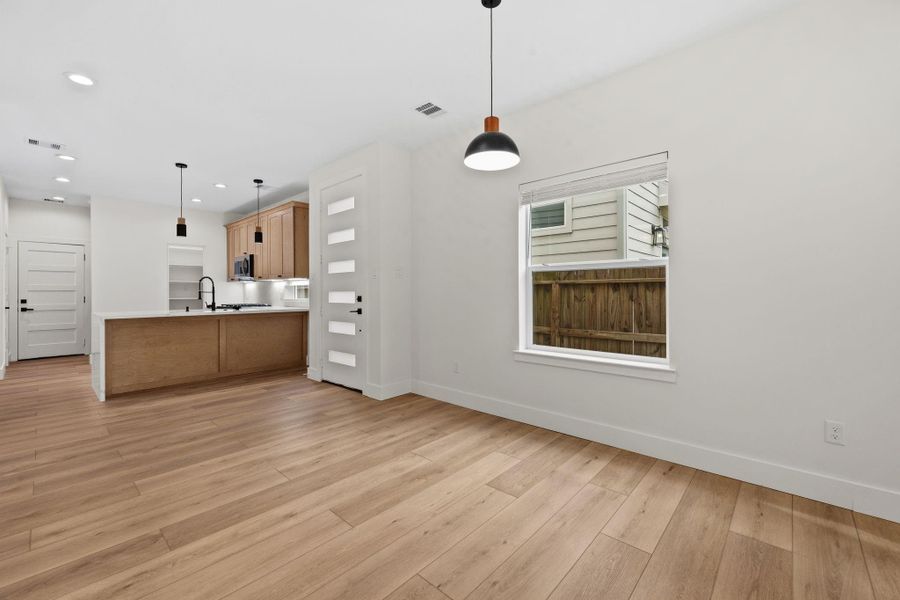 Bright and modern open-concept space featuring sleek wood floors, a stylish kitchen with pendant lighting, and a large window for natural light.