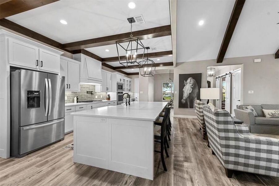 Kitchen featuring white cabinetry, stainless steel appliances, a barn door, beamed ceiling, and custom range hood