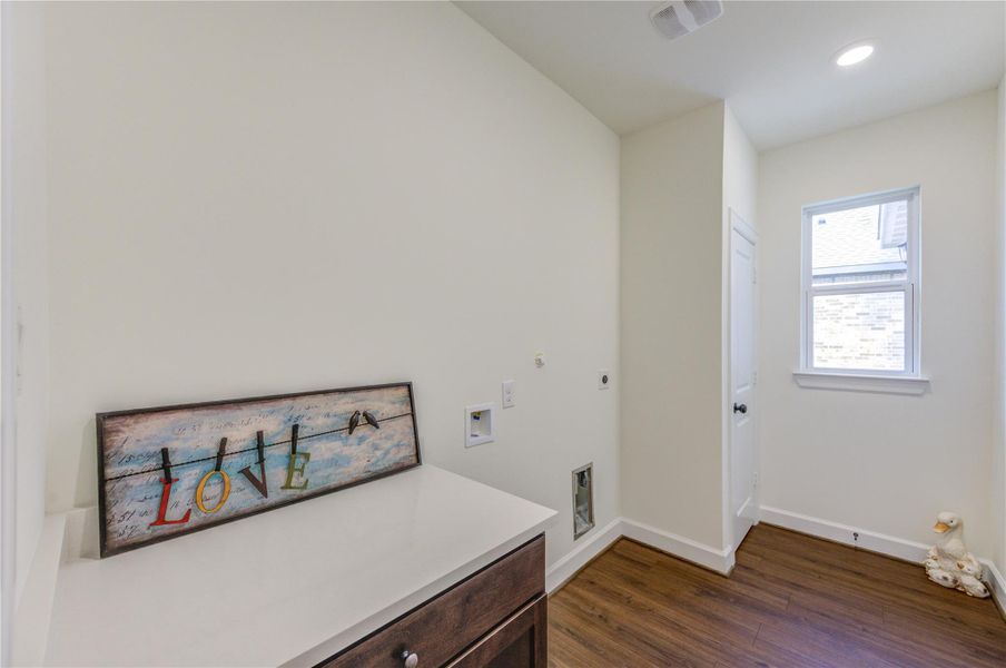 This photo shows a bright utility room with a window, featuring wood-style flooring and light walls. There's space for laundry appliances.