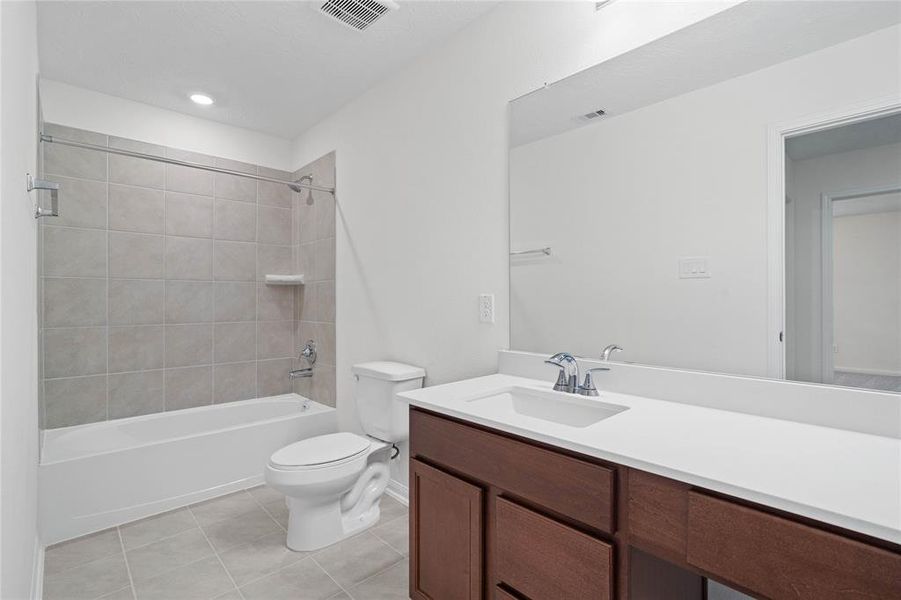 Secondary bath features tile flooring, bath/shower combo with tile surround, stained wood cabinets, beautiful light countertops, mirror, sleek fixtures and modern finishes.