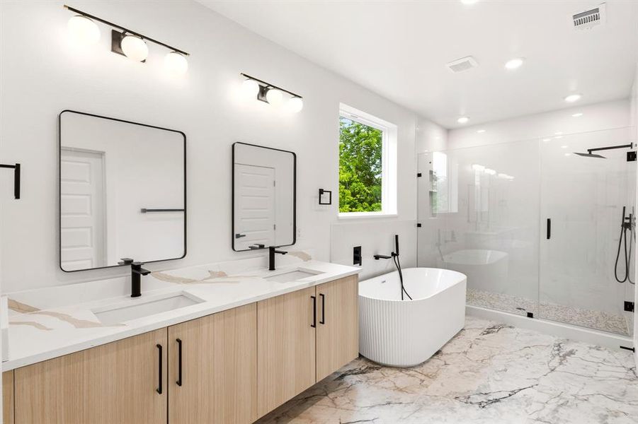 This bathroom features a double vanity with light wood cabinetry and white countertops, illuminated by modern wall-mounted light fixtures