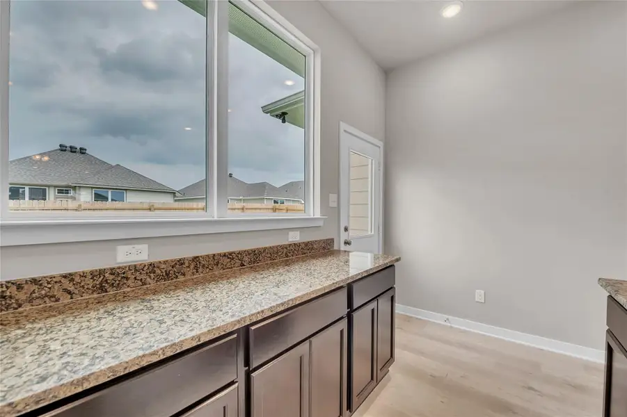 Bar area featuring light stone countertops, light wood finished floors, dark wood finish cabinets, and recessed lighting