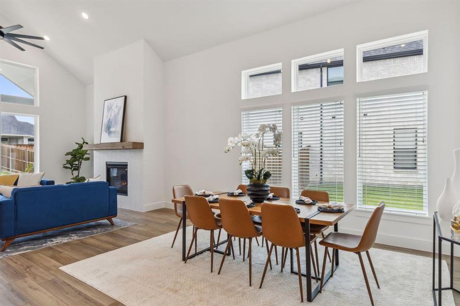 Dining room featuring high vaulted ceiling, a tiled fireplace, ceiling fan, and hardwood / wood-style floors