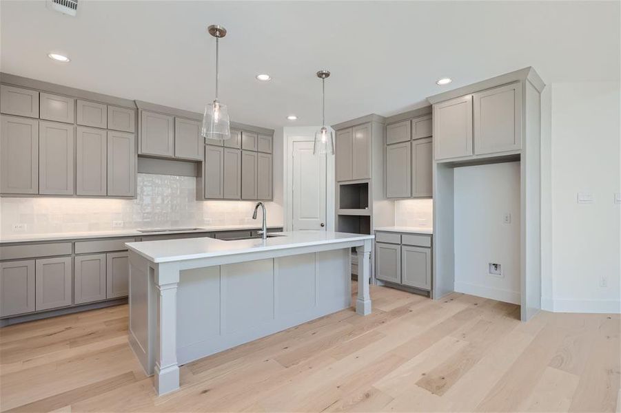 Kitchen with light wood-type flooring, backsplash, an island with sink, decorative light fixtures, and sink