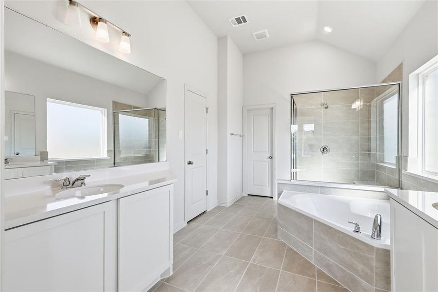 Bathroom with two vanities, a bath, a shower stall, light tile patterned flooring, and vaulted ceiling