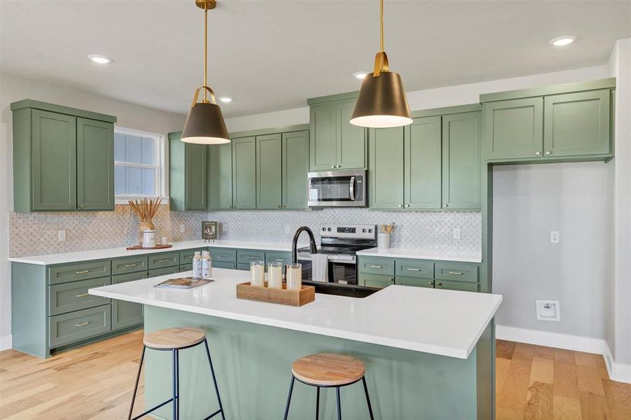 Kitchen featuring green cabinetry, a breakfast bar area, a center island with sink, appliances with stainless steel finishes, and recessed lighting Kitchen featuring green cabinetry, a breakfast bar area, a center island with sink, appliances with stainless steel finishes, and recessed lighting