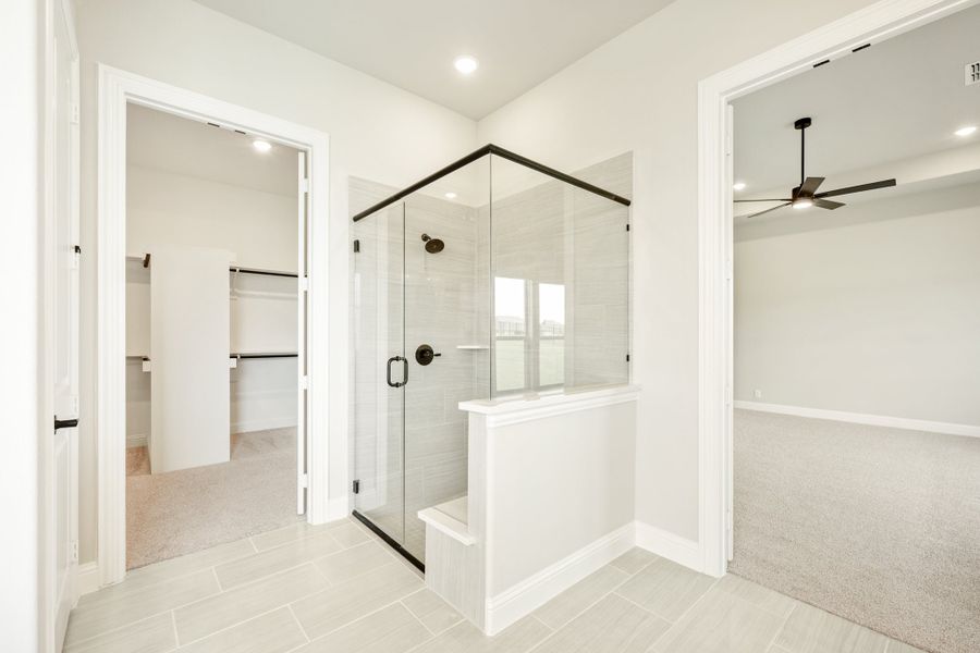 Master bathroom with glass walk-in shower, tile floors, and views into walk-in closet and bedroom with ceiling fan. Master bathroom with glass walk-in shower, tile floors, and views into walk-in closet and bedroom with ceiling fan.