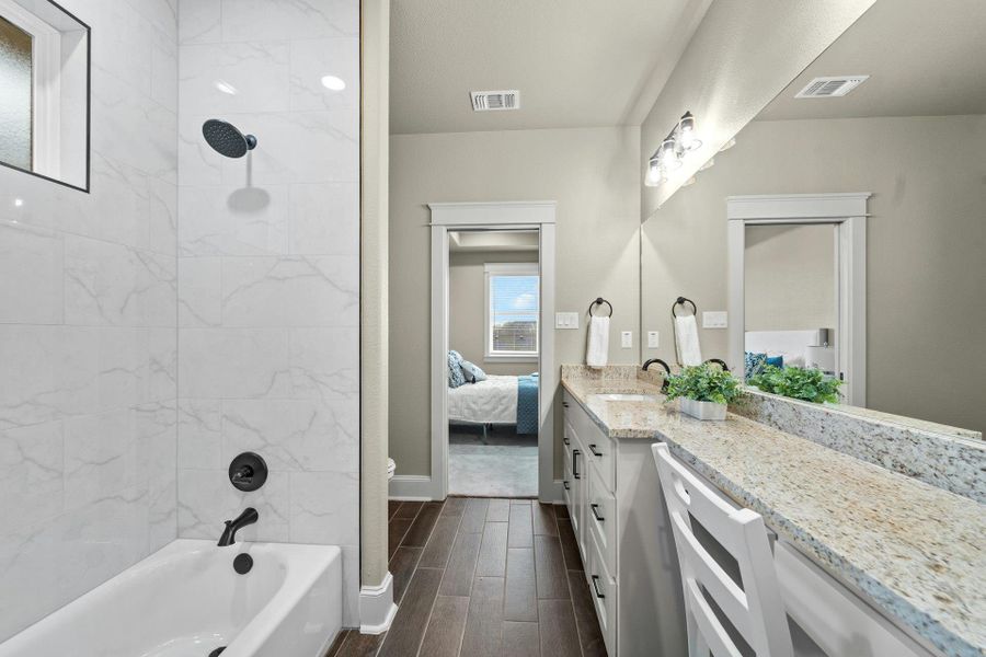 Bathroom featuring a dual vanity with granite-style countertops, white cabinetry, and matte black fixtures