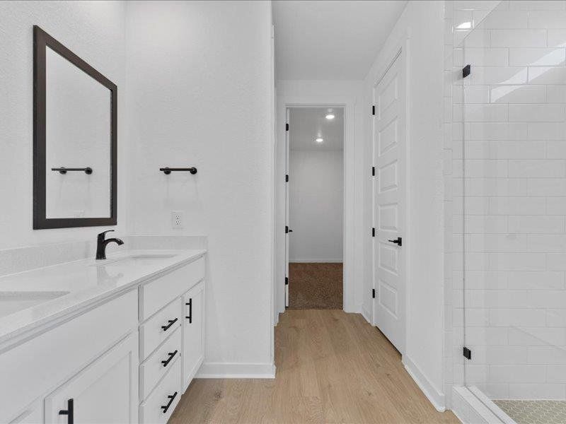Full bathroom featuring double vanity, a stall shower, and light wood-style floors