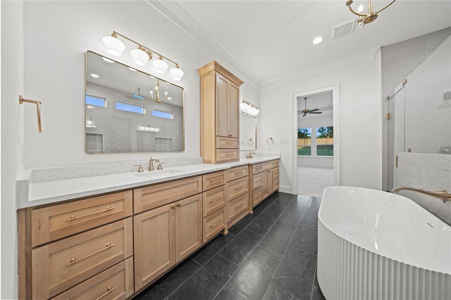 Full bath featuring a stall shower, double vanity, a freestanding tub, ornamental molding, and a ceiling fan