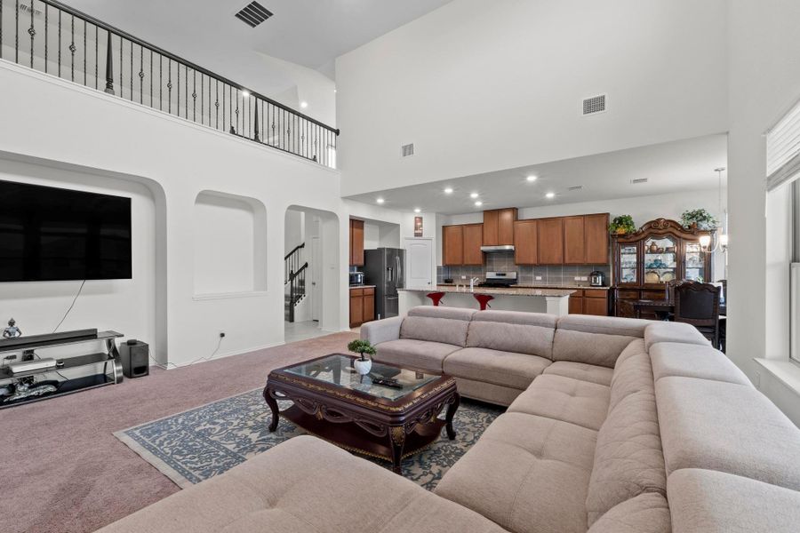 Vaulted living room featuring a second-story balcony with wrought iron railing, arched wall cutouts, recessed lighting, and an open concept kitchen